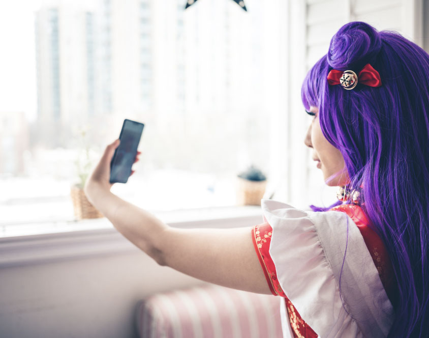 Anime cosplay girl with long purple hair taking a selfie with her phone.